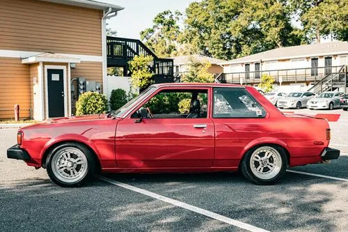 Front driver side view of a red 1980 Toyota Corolla two-door sedan showcasing its classic design and aftermarket wheels