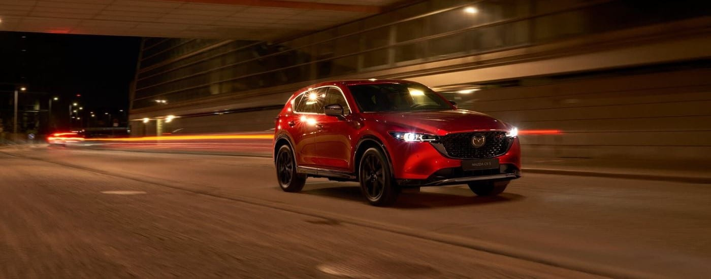 A red 2023 Mazda CX-% is shown driving at night.