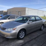 Front side view of a 2003 Toyota Camry LE, parked in a lot, showcasing its clean lines and original factory wheels.