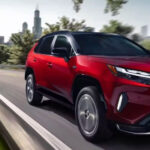 A red 2023 Toyota RAV4 Prime is shown driving near a city.