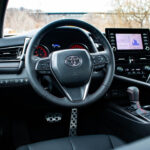 Side profile of the 2024 Toyota Camry TRD V6, highlighting the red TRD side skirts, black wheels, and sporty stance.