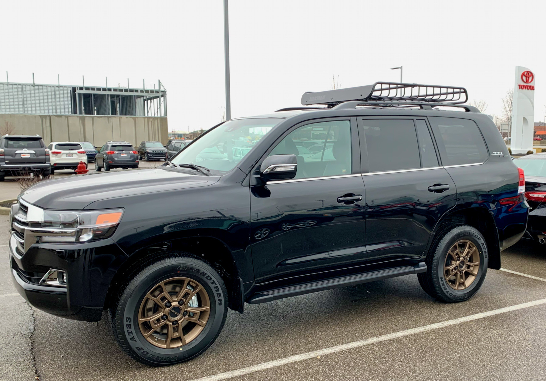 Midnight black 2021 Toyota Land Cruiser Heritage Edition parked in front of a Toyota dealership, showcasing its side profile and OEM running boards.