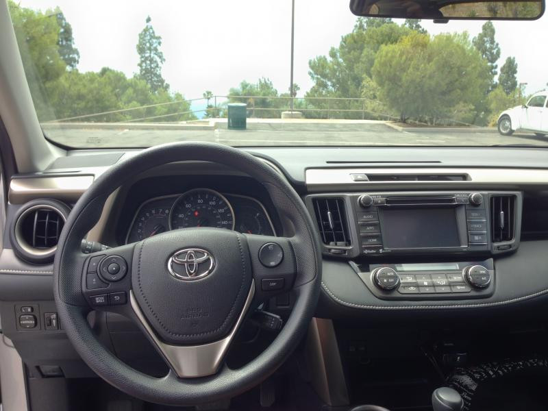 Steering wheel of the 2015 Toyota RAV4, showcasing a three-spoke design. The alt text is: 2015 Toyota RAV4 XLE steering wheel with controls.