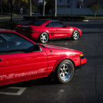 Two classic Toyota sports cars, a red AE86 and a red MR2, parked side by side.