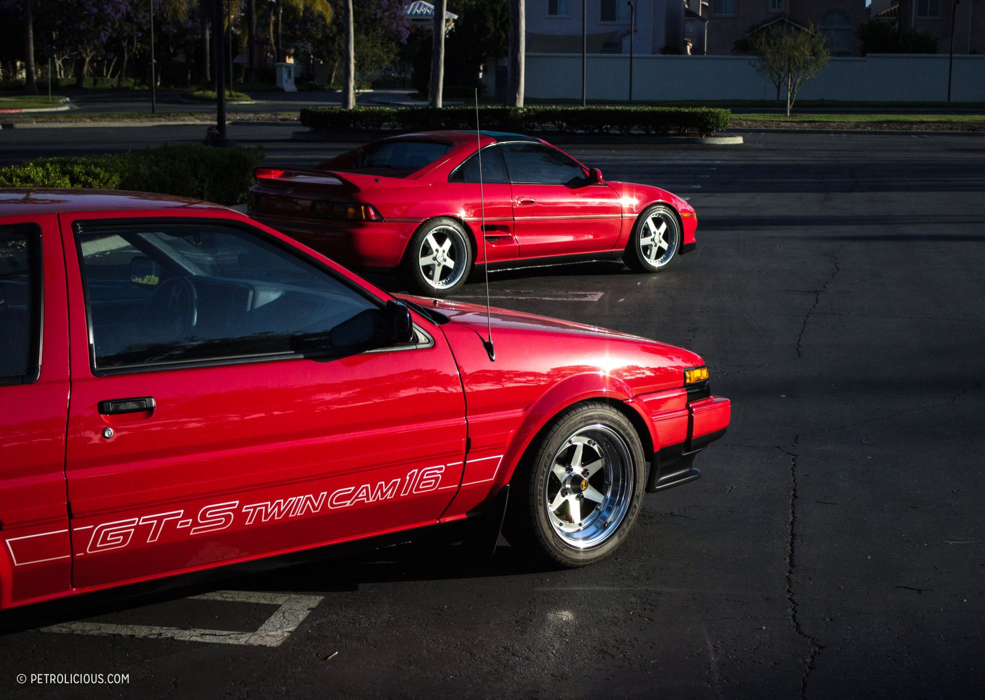 Two classic Toyota sports cars, a red AE86 and a red MR2, parked side by side.