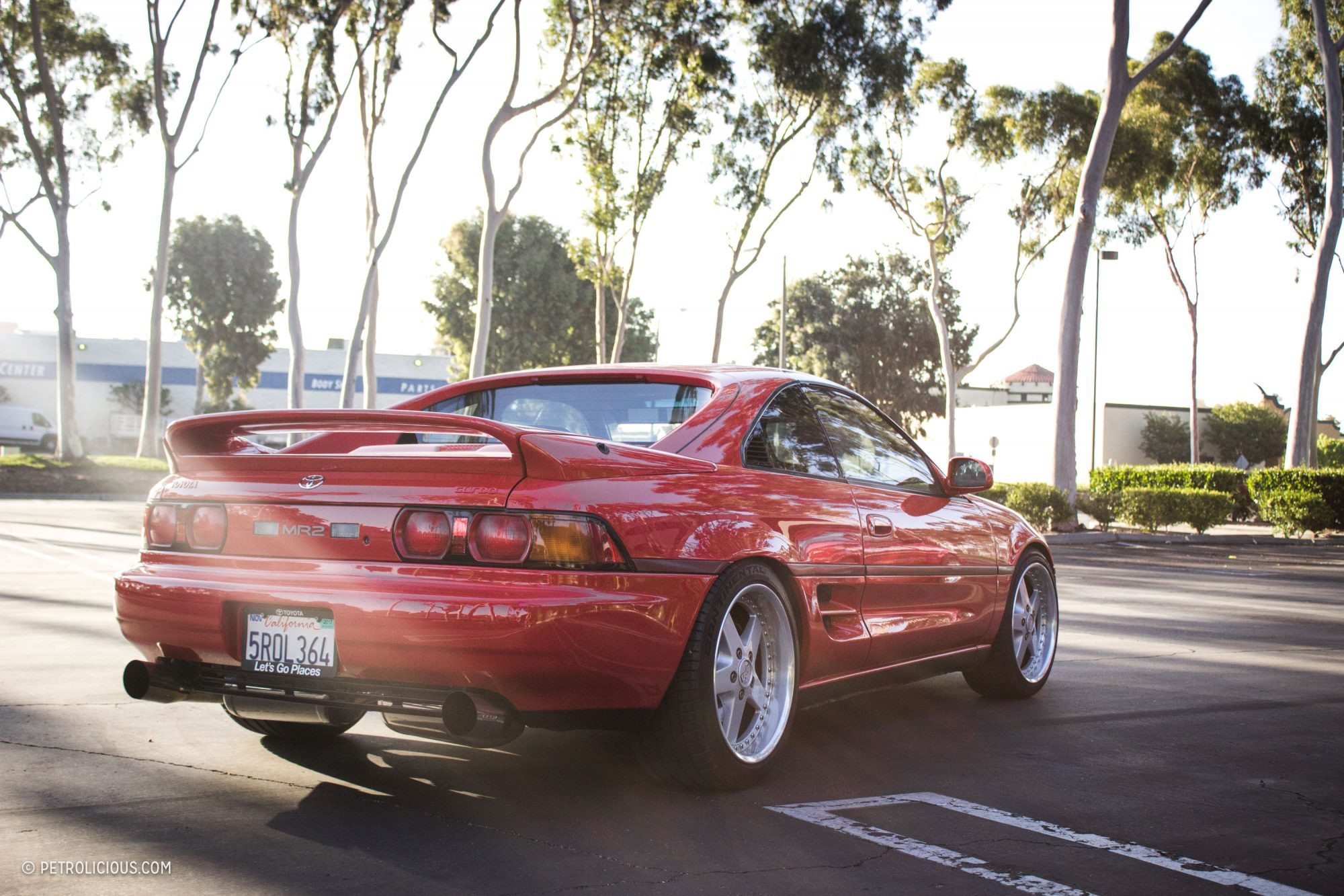 The rear of a red MR2 Turbo, showcasing its sleek design and aftermarket Work Equip wheels.