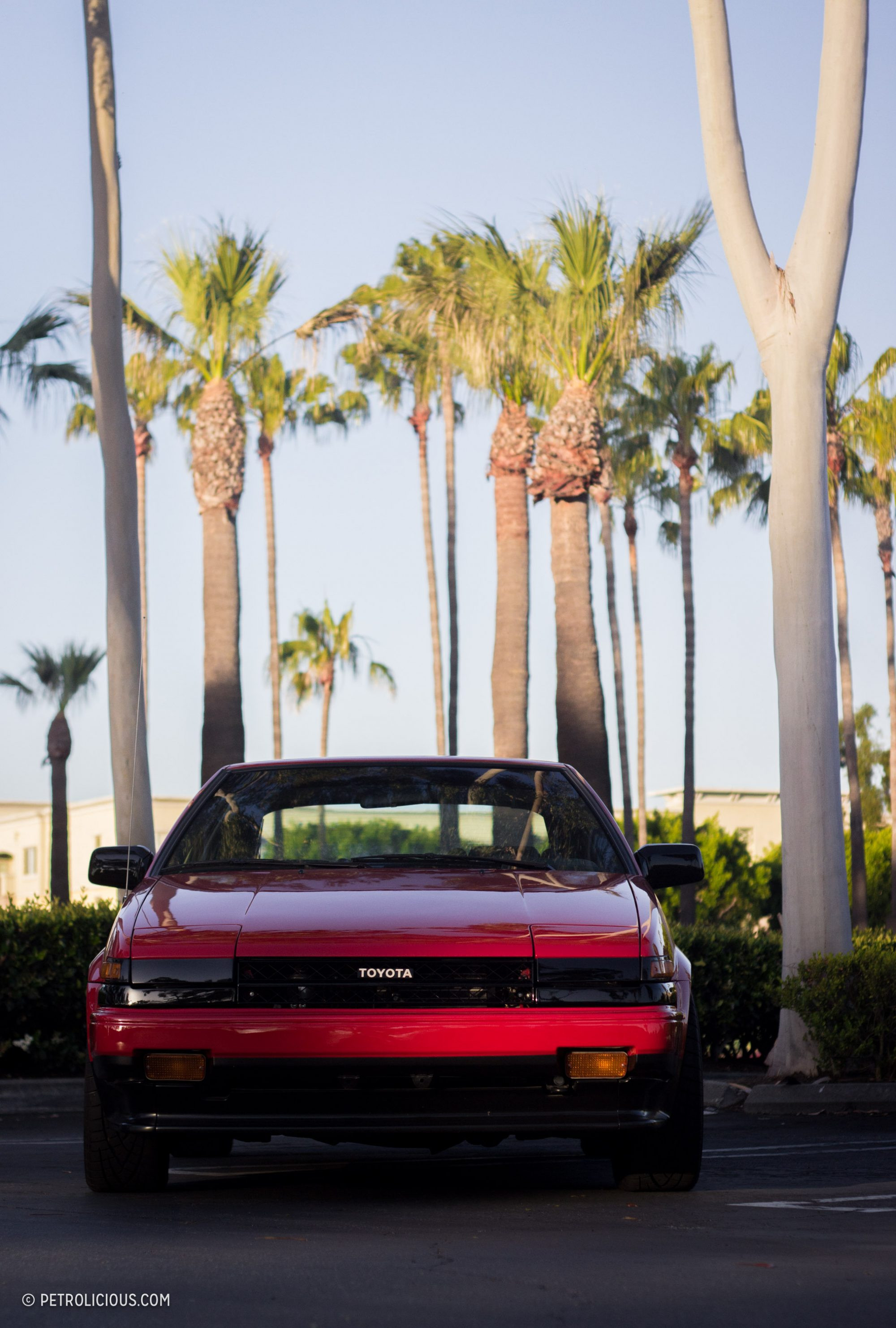 A close-up of the front of a red AE86, highlighting its pop-up headlights and iconic design.