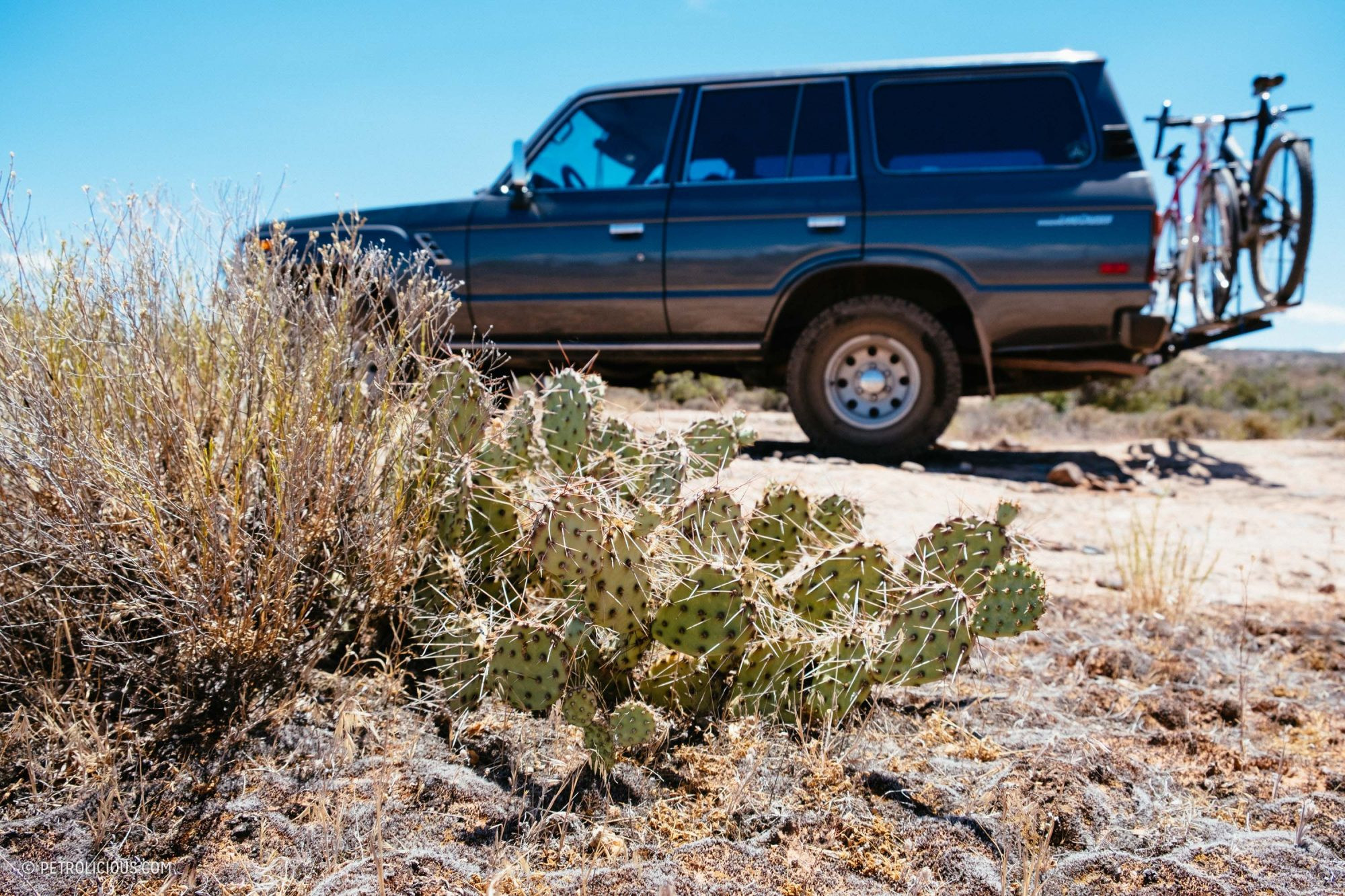 Front view of a red Toyota Land Cruiser parked in a desert town, showcasing its rugged front grille