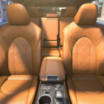 Luxurious car interior with tan leather seats featuring diamond stitching. Sunlight casts warm shadows, highlighting the modern and elegant design.