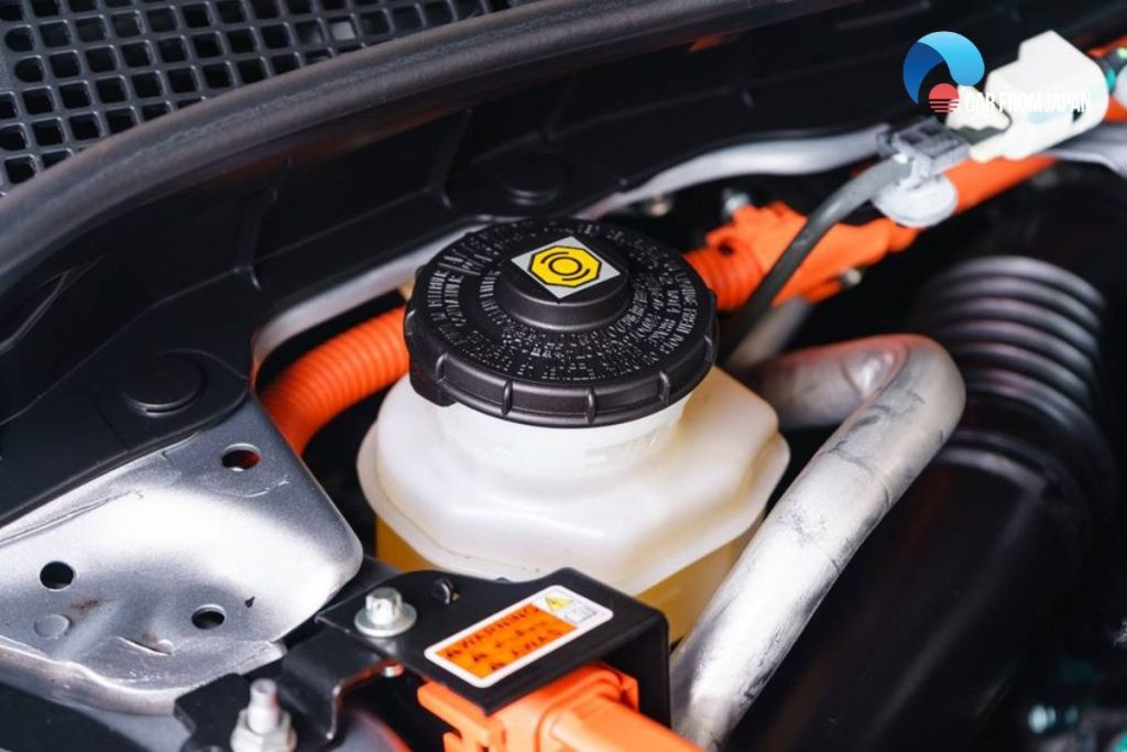 Brake fluid reservoir under the hood of a car showing the process of removing old fluid with a syringe