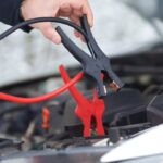 Black and red jumper cables being attached to a car battery